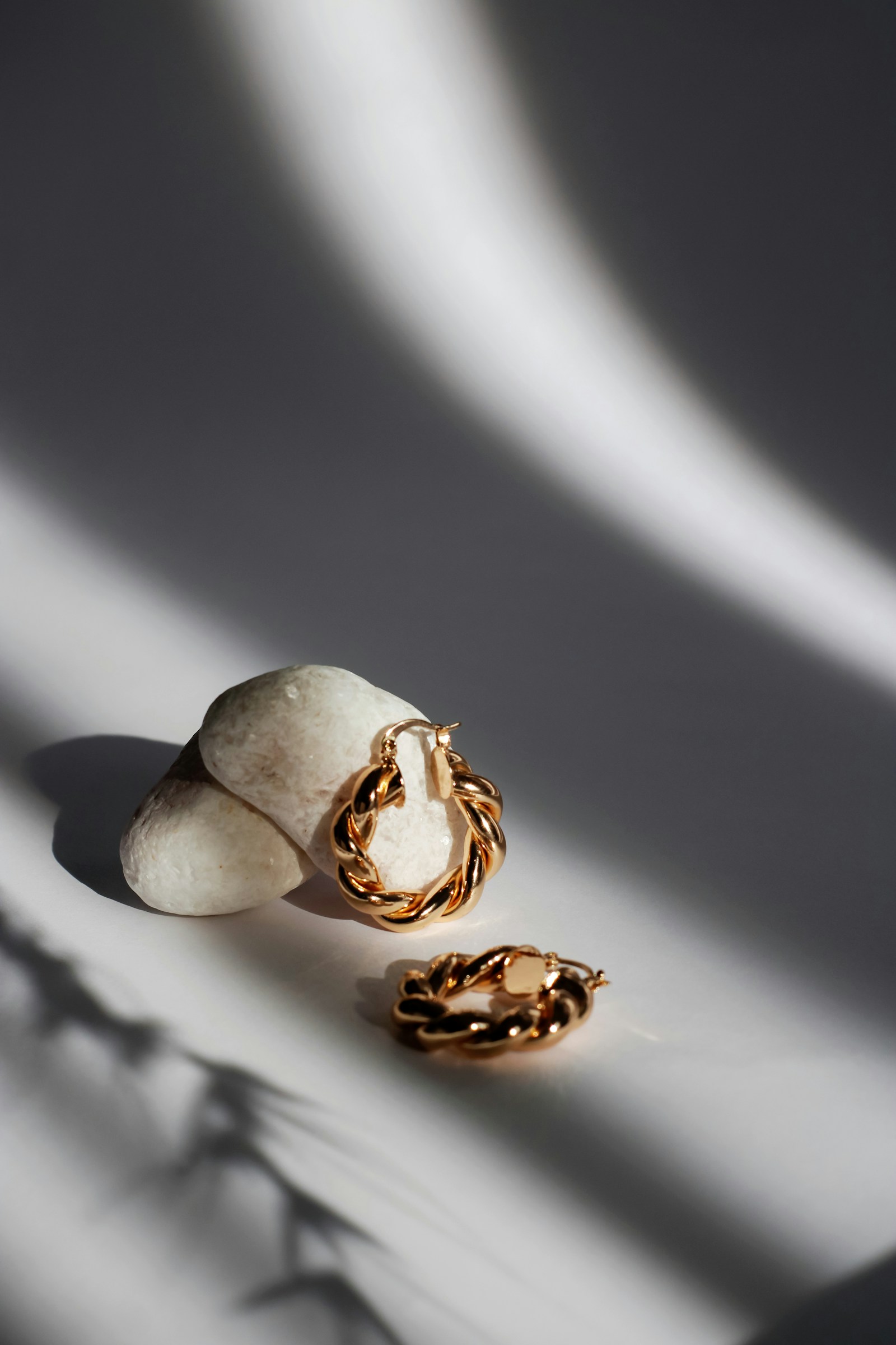 Sculptural gold hoop earrings resting on stone